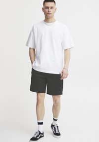 T-shirt blanche en coton à manches courtes, associée à un short noir. Détails notables : accents noirs et baskets noir et blanc.