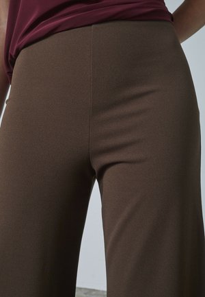 Bruna tygleggings med en slät yta och åtsittande design, med hög midja och utan synlig hårdvara eller mönster.