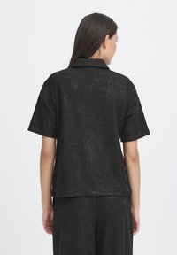 Camicia nera con trama, maniche corte e collo con rever. Caratterizzata da una vestibilità ampia e tessuto intrecciato, vista dalla parte posteriore.