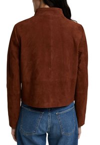 Bruin suède cropped jack met een hoge kraag en lange mouwen, met een gladde textuur en minimale stikdetails. Draagt met blauwe jeans.