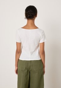 Valge lühikeste varrukatega pluus laia kaelusega, millele on lisatud oliivrohelised tekstuuriga püksid, millel on tagataskud ja mugav lõige.