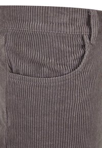 Grijs corduroy stof met verticale ribbelstructuur. Heeft een zijzak en een gestikte tailleband, wat de duurzaamheid en structuur benadrukt.