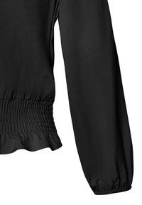Schwarze Bluse mit langen Ärmeln, die einen gerafften Bund und einen volanten Saum hat. Glatte Textur, leichtes Material und minimale Designdetails.