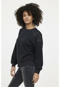 Sweatshirt noir avec des accents cloutés sur les épaules, col rond et poignets côtelés. Assorti avec un jean ajusté gris foncé. Matériau en mélange de coton.