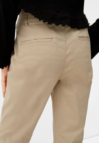 Beiga bomullshanter med en slät yta, med två bakfickor. Midjebandet är något texturerat.