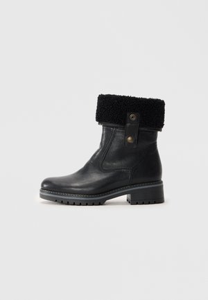 Botas de tobillo de cuero negro con un puño de borreguillo negro texturizado y un cierre de presión lateral. Presentan una suela de goma gruesa para mayor tracción.