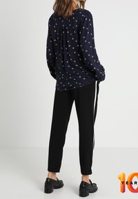 Marinebluse mit weißem Blumenmuster, langen Ärmeln und Rückenschlitzen, kombiniert mit schwarzen Hosen und schwarzen Schuhen mit dicker Sohle.