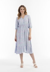 Rochie de culoare violet deschis cu imprimeu floral, decolteu în V, închidere cu nasturi, talie elastică și volan în straturi. Purtați cu sandale albe cu toc pătrat.