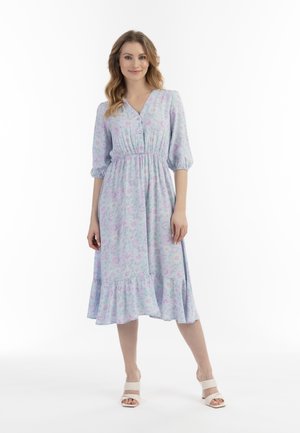 Rochie de culoare violet deschis cu imprimeu floral, decolteu în V, închidere cu nasturi, talie elastică și volan în straturi. Purtați cu sandale albe cu toc pătrat.