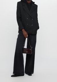 Blazer doppiopetto a scacchi neri sopra un felpa nera, abbinato a jeans larghi scuri e una piccola borsa bordeaux. Scarpe nere flat.