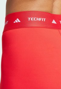 Czerwone szorty sportowe wykonane z elastycznego materiału, o dopasowanym kroju. Posiadają szeroką, markową elastyczną talię z napisem "TECHFIT" w kolorze białym.