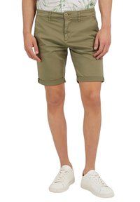 Pantalones cortos verde oliva con dobladillo vuelto, hechos de una tela ligera. Presentan un cierre de cremallera en la parte delantera y un botón, combinados con zapatillas blancas.
