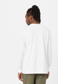 T-shirt bianco a maniche lunghe in morbido tessuto con collo rotondo e vestibilità rilassata. Presenta un piccolo dettaglio decorativo all'orlo inferiore.