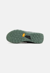 Sola di scarpa sportiva nera con un battistrada a motivo verde e un logo Vibram giallo. Presenta tacche angolari per aderenza e stabilità.