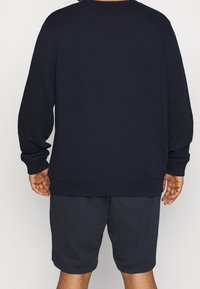 Felpa di cotone navy con maniche lunghe e polsini a costine, abbinata a pantaloni corti scuri. Presenta un collo rotondo e una vestibilità rilassata.