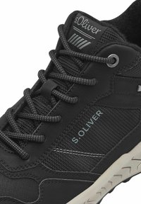 Černá sportovní bota s texturovaným svrškem, síťovanými akcenty, výrazným logem a gumovou podrážkou s dezénem pro trakci.