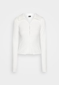 Camicia bianca a maniche lunghe in tessuto a coste con colletto, dotata di chiusura con bottoni e design a occhiello sul petto, vestibilità aderente e tessuto testurizzato.