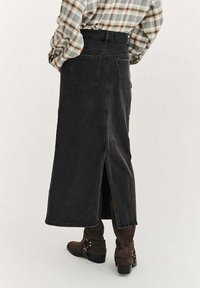 Čierna rifľová sukňa s rozparkom vzadu, dvoma zadnými vreckami a vysokým pásom, v kombinácii s hnedými čižmami a károvanou košeľou.