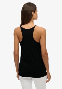 Zwart tanktop met een uitgesneden rug, gemaakt van zachte stof. Heeft dunne bandjes en een rechte zoom, gecombineerd met witte broek.