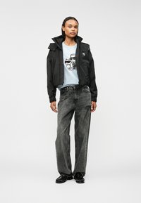 Juodas trumpas švarkas su gobtuvu, derinamas su šviesiai mėlynu marškinėlių su katėmis, pilkais laisvais džinsais ir blizgiais juodais batais.