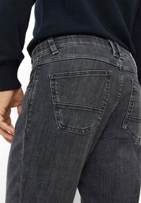 Jeans da uomo in denim grigio scuro con un design aderente, dotati di due tasche posteriori, cuciture sottili e una texture liscia.