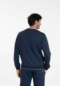 Sweatshirt bleu marine avec un col rond, des poignets et un ourlet côtelés. Présente une texture subtile et un accent contrastant au bas.