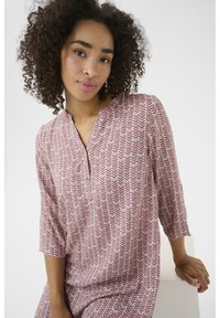 Blouse à motifs rose et blanc avec un décolleté en V, des manches trois-quarts et un design en zigzag. Tissu léger au toucher doux.