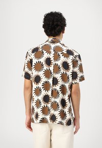 Camicia a maniche corte con sfondo crema e motivo a sole in marrone e nero. Realizzata in tessuto leggero e traspirante.