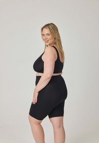 Czarny sportowy biustonosz i szorty do połowy uda. Gładka faktura, regulowane ramiączka oraz wysoki stan z minimalną ilością szwów.