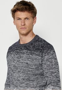 Grijze en marineblauwe gebreide trui met een gestructureerd patroon. Voorzien van een ronde hals en lange mouwen. Materiaal lijkt zacht en casual.