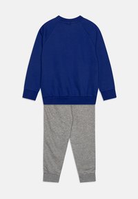 Sudadera azul de manga larga con puños acanalados, combinada con pantalones de chándal grises, ambos hechos de un suave y elástico tejido de algodón.