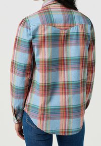 Rutig skjorta i blått, med vertikala och horisontella ränder i röd, grön och orange. Knappar vid ärmslut och rundad nederkant. Tillverkad av bomull.