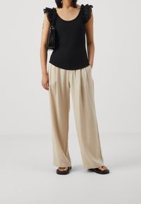 Svart linne med volangärmar, parat med lösa, beige byxor och svarta slip-on sandaler. Accessoarer inkluderar en liten svart handväska.