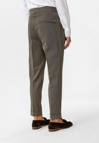 Bruine, gestreepte broek met een slim fit, opgerolde zomen en een achterzakdetail, gecombineerd met donker schoeisel.