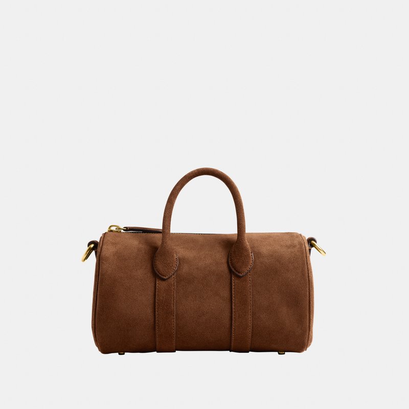 Sac cylindrique en daim marron avec deux poignées et une fermeture éclair et des accessoires dorés sur un fond clair et uni.