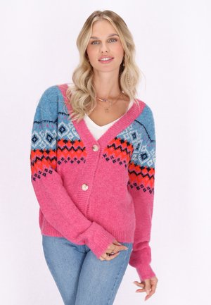 Roze cardigan met blauwe patroonmouwen die geometrische ontwerpen in oranje, zwart en wit tonen. Voorzien van knoopsluiting en lange mouwen.