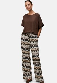 Brown short-sleeve top paired with loose-fitting, patterned pants featuring zigzag stripes in black, white, and earthy tones.