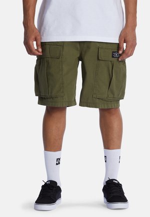 Shorts cargo vert olive avec plusieurs poches latérales, présentant un tissu texturé et une coupe décontractée, portés avec des chaussures noires et des chaussettes blanches.