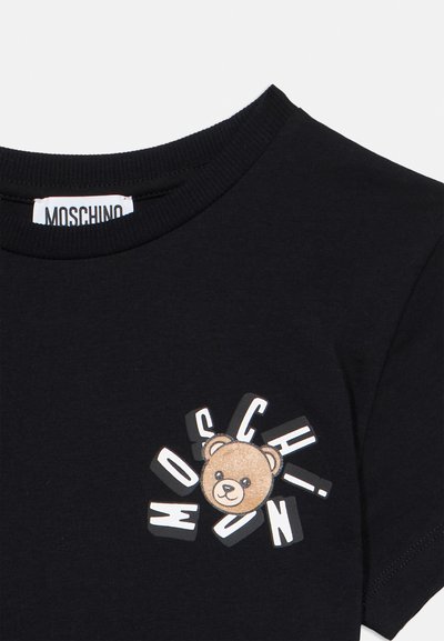 Μαύρο T-shirt με πρόσωπο αρκουδάκι και διάσπαρτα λευκά γράμματα που σχηματίζουν τη λέξη "MOSCHINO" στο στήθος κάτω από το λαιμό.