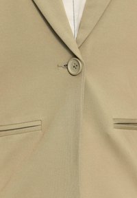 Bruine blazer met een enkele knoopsluiting, dubbele voorzakken, notch revers en een subtiele textuur. Eenvoudig en strak ontwerp.