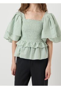 Grön och vit rutig blus med puffärmar, smockad kropp och volangkant. Lättviktigt bomullstyg. Fyrkantig halsringning.