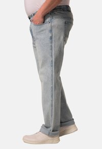 Jeans de mezclilla azul claro con un corte relajado, diseño de cinco bolsillos y puños enrollados. Combinados con zapatillas deportivas beige sobre un fondo liso.