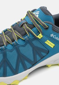 Modrá a šedá sportovní bota s síťovým svrchem, texturovanými detaily, jasně žlutými akcenty a šedými tkaničkami. Má robustní, lehkou podrážku.