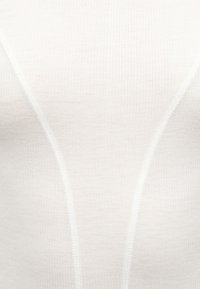 Κοντινή λήψη λευκόυ ριγωτού υφάσματος με κάθετες ραφές που σχηματίζουν ένα διακριτικό σχέδιο κλεψύδρας.