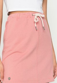Saia rosa com cordão, feita de tecido macio, apresentando uma cintura com um cordão de cor creme e um pequeno logotipo na barra.