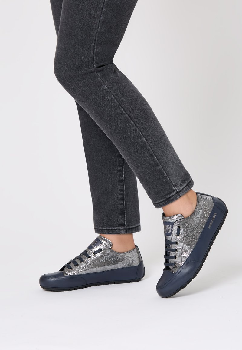 Sneaker con una toma superiore scintillante argentata e suola in gomma blu navy. Presenta lacci e marchio sul lato. Abbinati a jeans scuri.