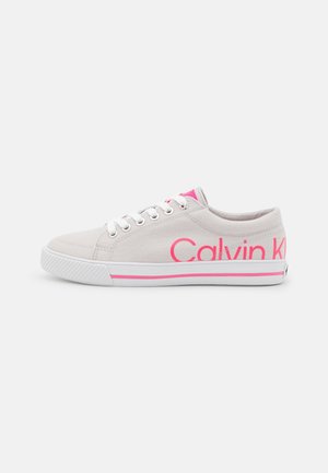 Zapatilla de lona beige baja con cordones blancos, detalles rosas y logo "Calvin Klein" en el lateral y suela de goma.