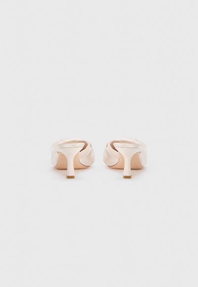 Mules à talons hauts en satin nude avec un design de talon sculpté et un tissu lisse. Bout arrondi avec une légère texture plissée à l'avant.