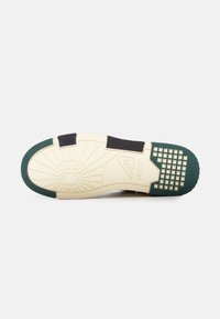 Sole della sneaker con una base crema spessa, accenti in gomma verde, trazione a motivo e inserti neri per supporto.
