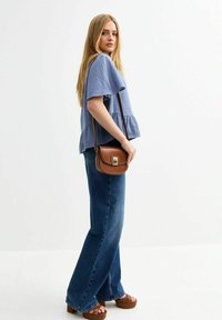Ljusblå kortärmad topp med peplumdesign, matchad med mörka jeans med utsvängda ben och en brun axelväska med lås. Bruna platåskor.